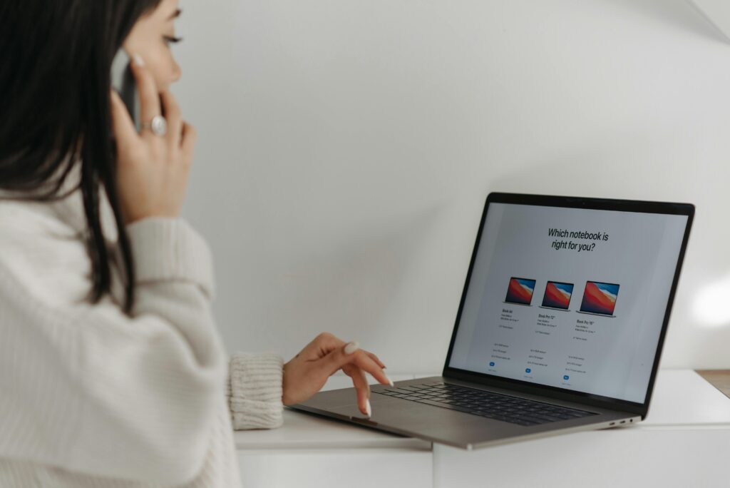 Asian woman on phone using laptop for online shopping against a white wall.